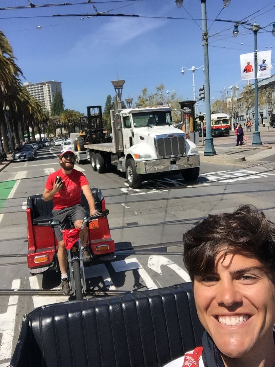 Geoff grinning from the back seat of a pedicab on the Embarcadero, with another Cabrio driver behind.